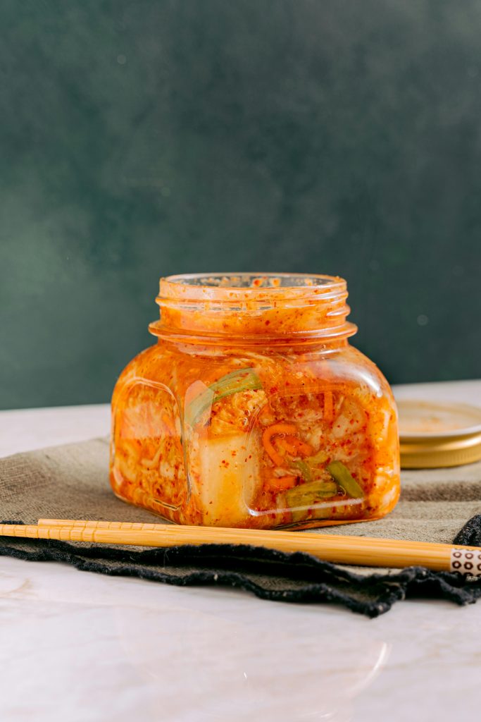 pexels-photo-6823267-6823267 Close-up of homemade kimchi in a jar with chopsticks on a table.